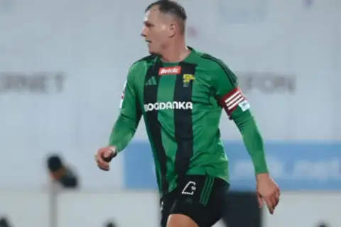 Piłkarz Górnika Łęczna w zielonej koszulce z czarnymi pasami, gotowy do gry przeciwko GKS Tychy.
