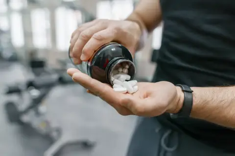 Mann schüttet weiße Pillen aus einer Flasche in seine Hand. Möglicherweise zur Unterstützung der Yohimbin Wirkung im Fitnessstudio.