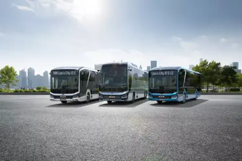 Trzy nowoczesne autobusy elektryczne MAN Lion's City E stoją na tle miejskiej panoramy.