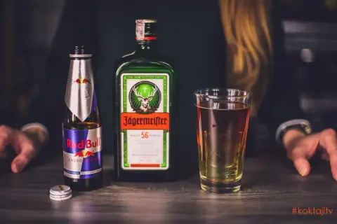 Jägermeister z czym pić? Klasycznie z Red Bullem, tworząc popularny "Jägerbomb". Na zdjęciu butelka Jägermeistera, puszka Red Bulla i gotowy drink.