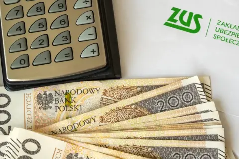 Kalkulator, banknoty 200 zł i logo ZUS. Obliczenia dotyczące tego, ile wynosi dodatek do emerytury za warunki szkodliwe.