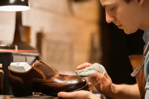 Un artisan applique du cirage pour chaussures sur un soulier en cuir marron, lui redonnant son éclat.