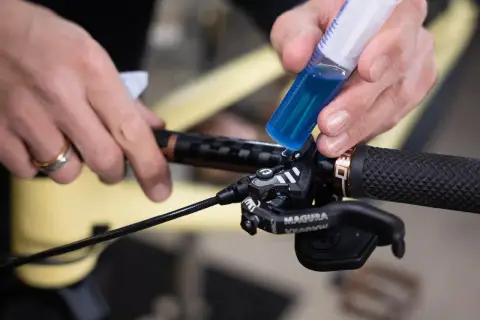 Hands add blue brake fluid from a syringe to a bicycle brake lever. This fluid is corrosive due to its hygroscopic nature, absorbing moisture.