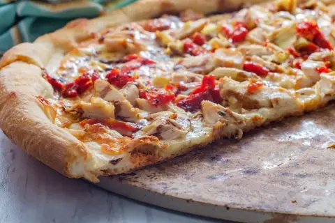 Kawałek domowej pizzy z kurczakiem i suszonymi pomidorami na kamieniu.