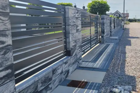 Nowoczesne ogrodzenie przed domem z szarego metalu i kamiennych bloczków, z bramą wjazdową i furtką.