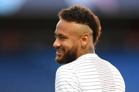 Sonrisa de Neymar con su característico peinado mohicano, luciendo una camiseta a rayas blancas y rojas.
