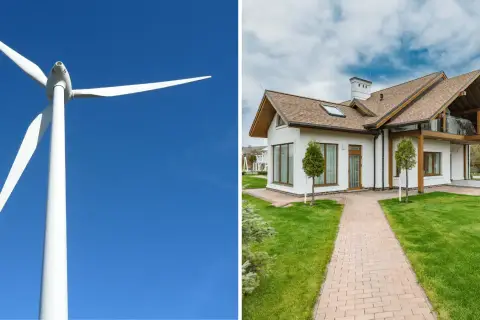 Biała turbina wiatrowa na tle błękitnego nieba obok nowoczesnego domu z zielonym trawnikiem.