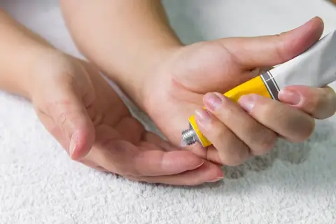 Manos aplicando crema de un tubo amarillo en la palma de otra mano.