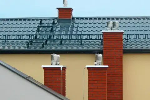 Dwa ceglane kominy z obrotowymi nasadami zapewniają sprawną wentylację w domu.