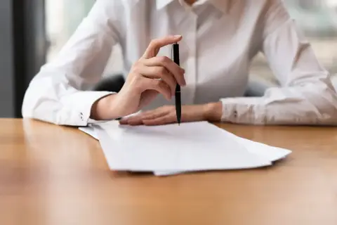 Dłoń z długopisem nad stosem papierów, przygotowująca skargę na kuriera InPost.