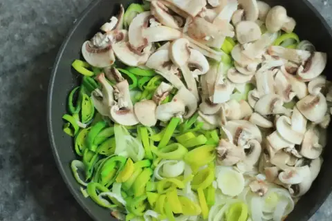 Kroimy pieczarki i pora na patelni, przygotowując składniki do pysznego sosu pieczarkowego.
