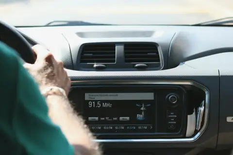 Ręce na kierownicy, radio samochodowe pokazuje 91.5 MHz. Wygodne środki masowego przekazu w podróży.