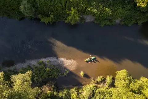 Dwie osoby płyną kajakiem po rzece w pobliżu Frysztaka, otoczeni bujną zielenią.