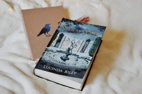 Książka "Siedem Sióstr" Lucindy Riley na tle okładki z ptakiem.