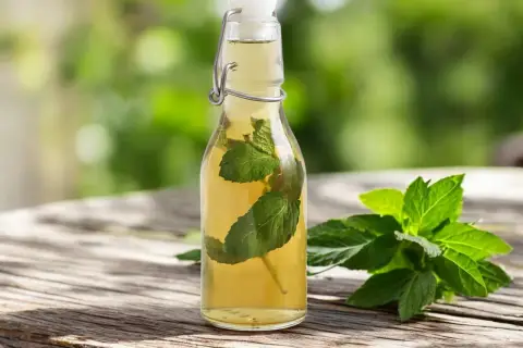 Bouteille de sirop de menthe maison avec des feuilles de menthe fraîche sur une table en bois.