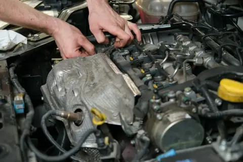 Mechanik pracuje przy silniku, sprawdzając czujnik położenia wałka rozrządu. Objawy awarii mogą być różne, od nierównej pracy po problemy z odpaleniem.