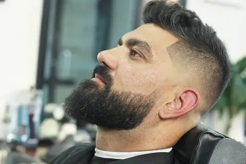 Hombre con barba y un moderno corte de pelo con degradado, uno de los tipos de corte de pelo hombre más populares.