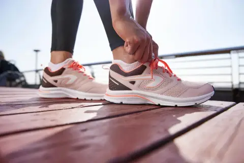 Dłoń zawiązuje sznurówki w różowych butach sportowych. Wyglądają na trochę za duże, ale gotowe do biegu.