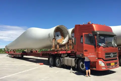 Ciężarówka transportuje łopatę turbiny wiatrowej. To ważny element w kraju tranzytowym, czekający na dalszą podróż.