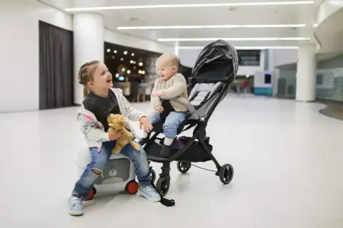 Dwie dziewczynki, jedna siedzi na walizce, druga w wózku, gotowe na podróż z Ryanair. Wózek dla 3 latka idealny na lotnisko.