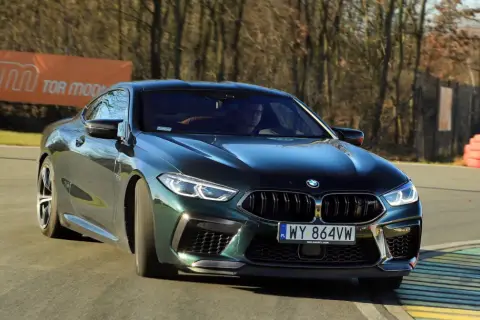 Mocne m8 bmw w ciemnozielonym kolorze na torze wyścigowym, z widocznym banerem "TOR MODLIN" w tle.