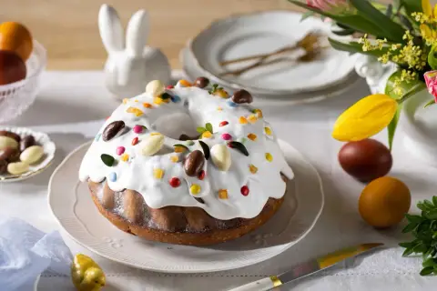 Wilgotna babka bez jajek, ozdobiona lukrem, kolorowymi drażetkami i czekoladowymi jajeczkami, na wielkanocnym stole.