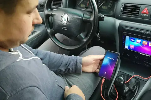 Mężczyzna w samochodzie podłącza telefon do radia, by uzyskać połączenie telefonu z samochodem. Na ekranie telefonu widnieje logo Weblink.