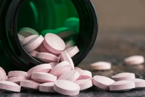 Różowe tabletki wysypują się z zielonego pojemnika. Wśród nich widać tabletki z chromem, które mogą pomóc w utrzymaniu prawidłowego metabolizmu.
