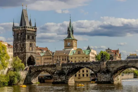 Most piękne stolice Europy, Most Karola w Pradze, z wieżami i zegarem, na tle błękitnego nieba z chmurami.