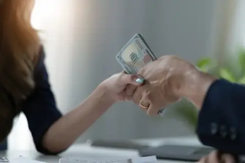 Dwie osoby przekazują sobie plik banknotów. To może być pożyczka od osoby prywatnej, która pomoże w nagłej potrzebie.