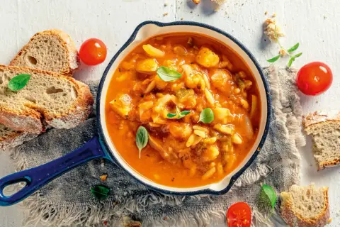 Eine dampfende, traditionelle italienische Suppe mit Gemüse und Pasta, serviert mit frischem Brot und Tomaten.