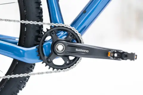 Widok z bliska na niebieski rower, z widoczną korbą Shimano i łańcuchem. Dowiedz się, jak odkręcić pedały w rowerze.