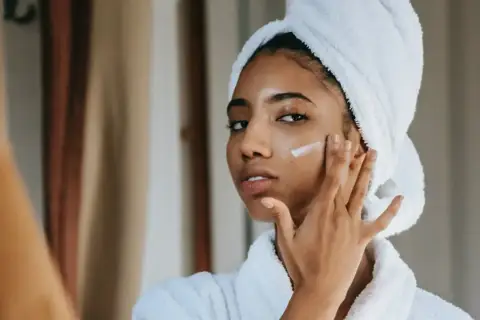 Mujer con toalla en la cabeza aplicándose crema para combatir la piel seca.