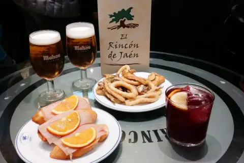 Dwa piwa Mahou, tapas z szynką i pomarańczą, smażone kalmary i sangria na stole w El Rincón de Jaén.