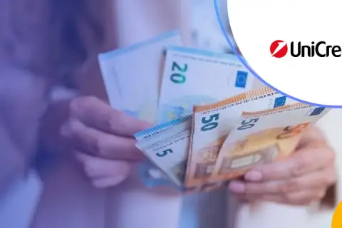 Dłonie trzymają banknoty euro, w tym 50 i 20 euro. Logo UniCredit sugeruje usługi bankowe.