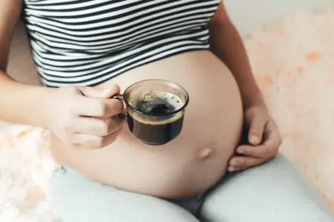 Kobieta w ciąży trzyma filiżankę kawy. Delikatny napój dla przyszłych mam.