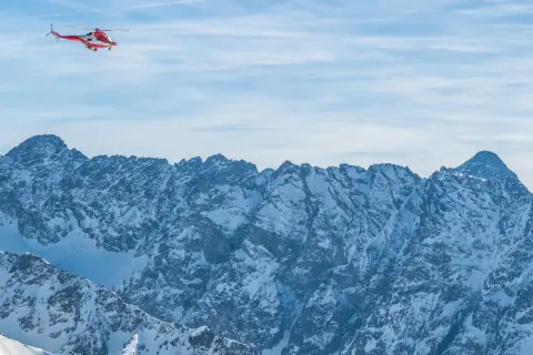 Czerwony helikopter ratunkowy lata nad ośnieżonymi Tatrami.