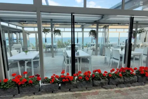 Letnia atmosfera przy plaży w Hotelu Lambert. Stoliki i krzesła czekają na gości, a morze w tle zaprasza do relaksu.