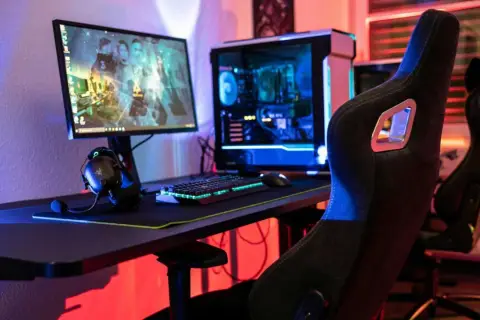 Gaming-Setup mit beleuchtetem PC, Tastatur und Kopfhörern. Der **Atlas OS**-Desktop zeigt ein Spiel.