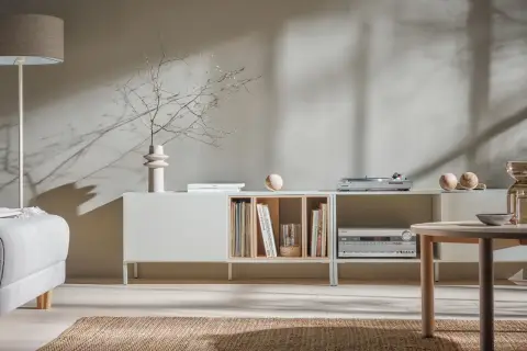 Miękkie światło pada na ściany w kolorze kaszmirowym, oświetlając salon z minimalistyczną komodą i wygodną sofą.