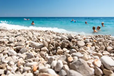 Kamienista plaża w Chorwacji, ludzie kąpią się w turkusowym morzu. Idealne miejsce na wakacje, gdzie nawet buty do Chorwacji nie są potrzebne, by cieszyć się słońcem.