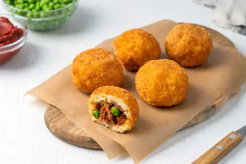 Arancini dorados y crujientes, uno cortado revela un relleno de carne y guisantes. ¡Una deliciosa receta arancini lista para disfrutar!