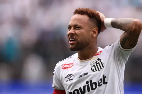 Neymar z grymasem na twarzy, trzymający się za głowę, sugeruje ból po kontuzji.