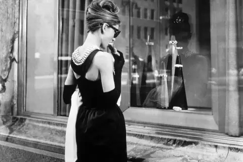 Audrey Hepburn, icónica en su vestido negro y perlas, disfruta de un pastel frente a Tiffany's.