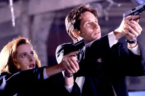 Z archiwum X: Scully i Mulder w akcji, celują z broni. Tajemnica czeka.