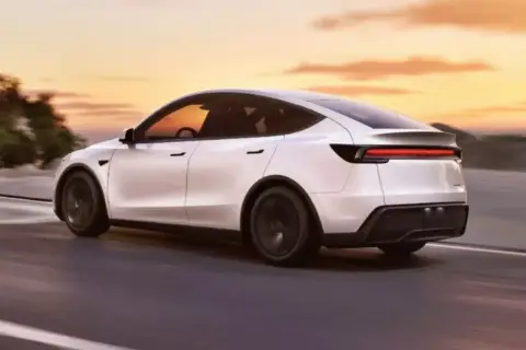 Biały Tesla Y 2025 pędzi po drodze o zachodzie słońca.