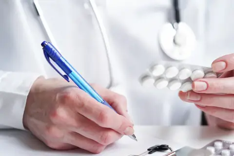 Lekarz przepisuje leki przeciwlękowe, trzymając blister tabletek i pisząc receptę.