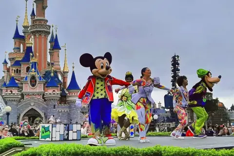Myszka Miki i przyjaciele tańczą na scenie w Disneylandzie przed zamkiem.