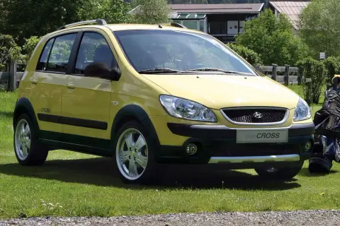 Żółty Hyundai Getz Cross zaparkowany na trawie obok torby golfowej.