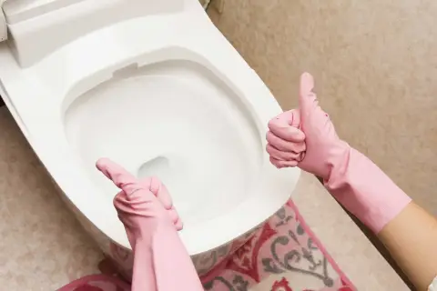 Ręce w różowych rękawiczkach pokazują kciuk w górę i wskazują na toaletę. Proste wskazówki, jak odetkać toaletę, gdy masz problem.